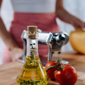 Close-up of olive oil, tomatoes, and pasta machine on a wooden board.
