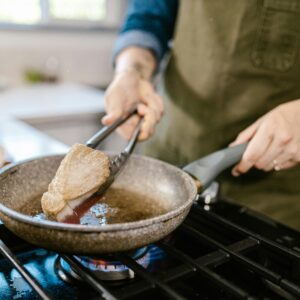 Close-up of a chef frying a tuna steak using tongs in a pan on a gas stove.