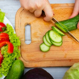 Fresh vegetables being sliced on a cutting board for a healthy meal prep.