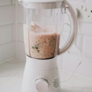 A white kitchen blender blending a fresh fruit and herb smoothie on a countertop.