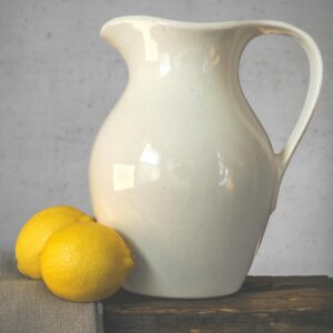Artistic still life of a porcelain jug with lemons on a rustic table.