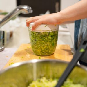 Close-up of a hand using a manual food chopper for herbs in a contemporary kitchen.