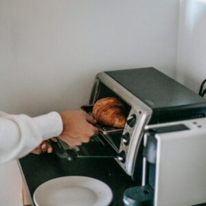 From above of crop anonymous person using microwave oven while heating yummy croissant for breakfast