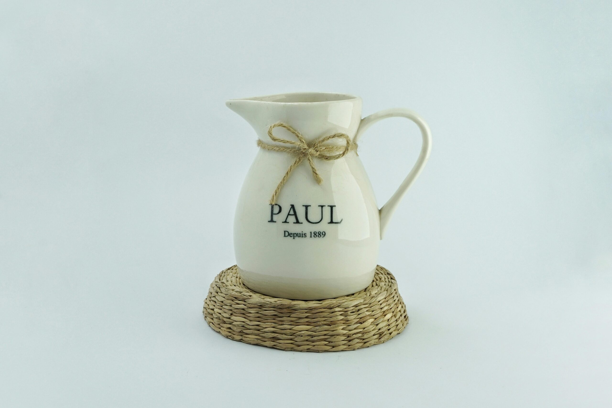 Elegant ceramic pitcher with a bow on a woven mat, perfect for minimalist decor.