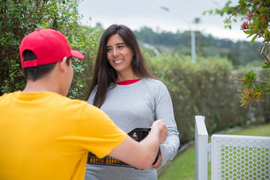 Smiling woman receives a package from a delivery man in a residential area outdoors.